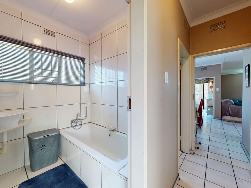 A functional bathroom featuring a bathtub and wall-mounted basin with tiled finishes, providing direct access to the adjacent living area.
