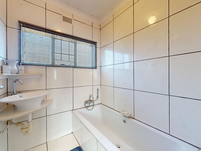 A compact bathroom featuring white wall tiles, a built-in bathtub, and a modern vessel sink with exposed plumbing.