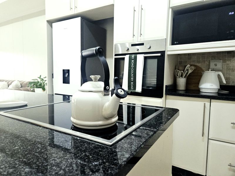 Modern kitchen featuring sleek white cabinetry, dark granite countertops, a built-in oven, and an integrated induction hob.