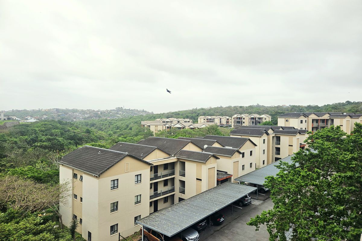 An elevated aerial view of a residential apartment complex featuring multi-story buildings, tiled roofs, and covered parking bays set within a landscaped environment.
