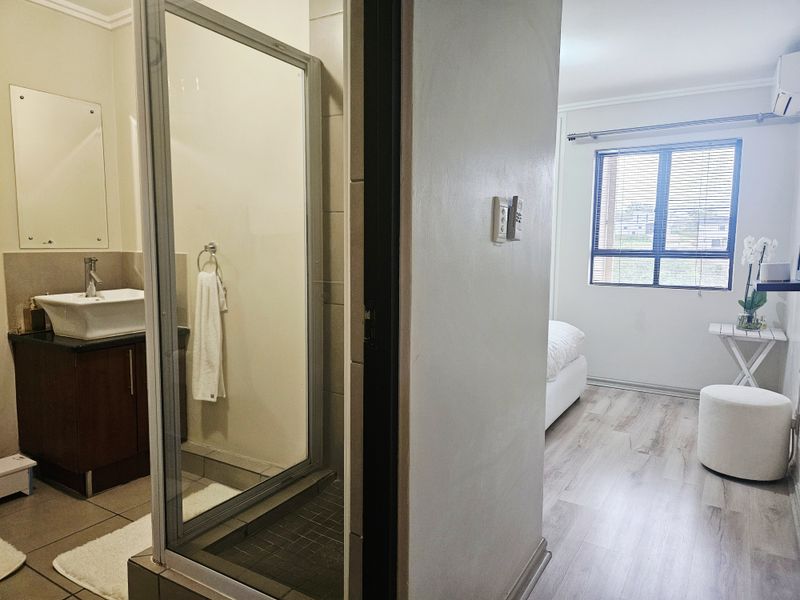 A bedroom featuring laminate flooring and an en-suite bathroom with a vanity cabinet, vessel sink, and glass-enclosed shower.