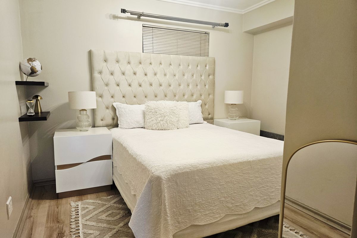 A well-maintained bedroom featuring neutral walls, laminate flooring, and a window fitted with venetian blinds.