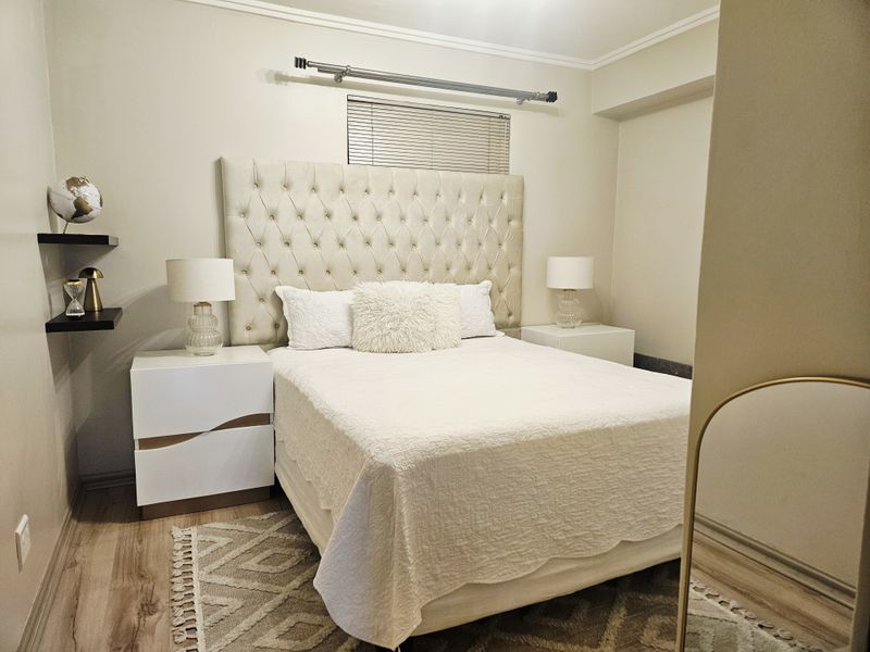 A well-maintained bedroom featuring neutral walls, laminate flooring, and a window fitted with venetian blinds.