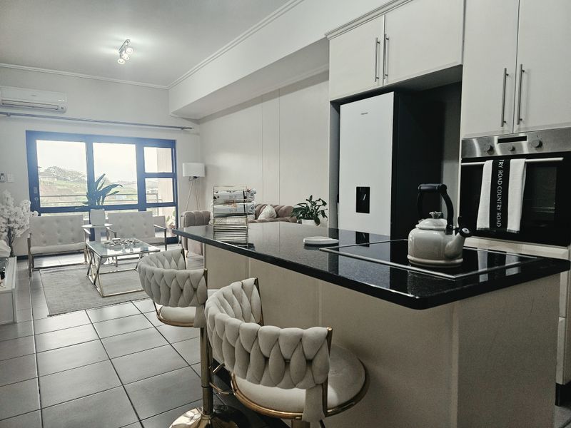 Modern open-plan apartment featuring a sleek kitchen with granite countertops, built-in oven, and seamless flow to the living area with balcony access.