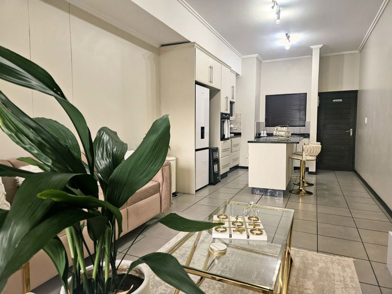 An open-plan living and kitchen area featuring tiled flooring, modern built-in cabinetry, a central kitchen island, and neutral wall finishes.