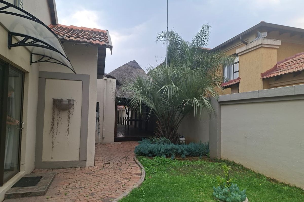 Rear garden area featuring a paved walkway, boundary wall, and a covered thatched outdoor entertainment space.