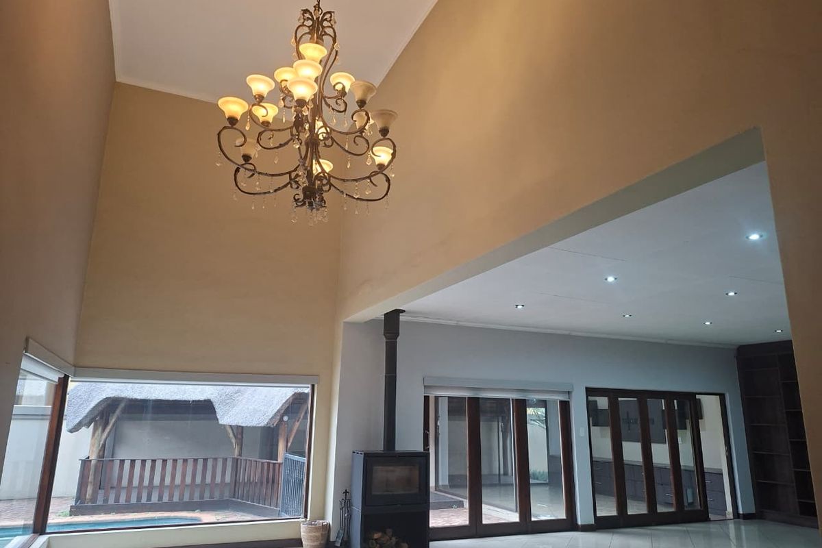 Spacious living area featuring high vaulted ceilings, a modern freestanding fireplace, large windows with garden views, and sleek tiled flooring throughout.