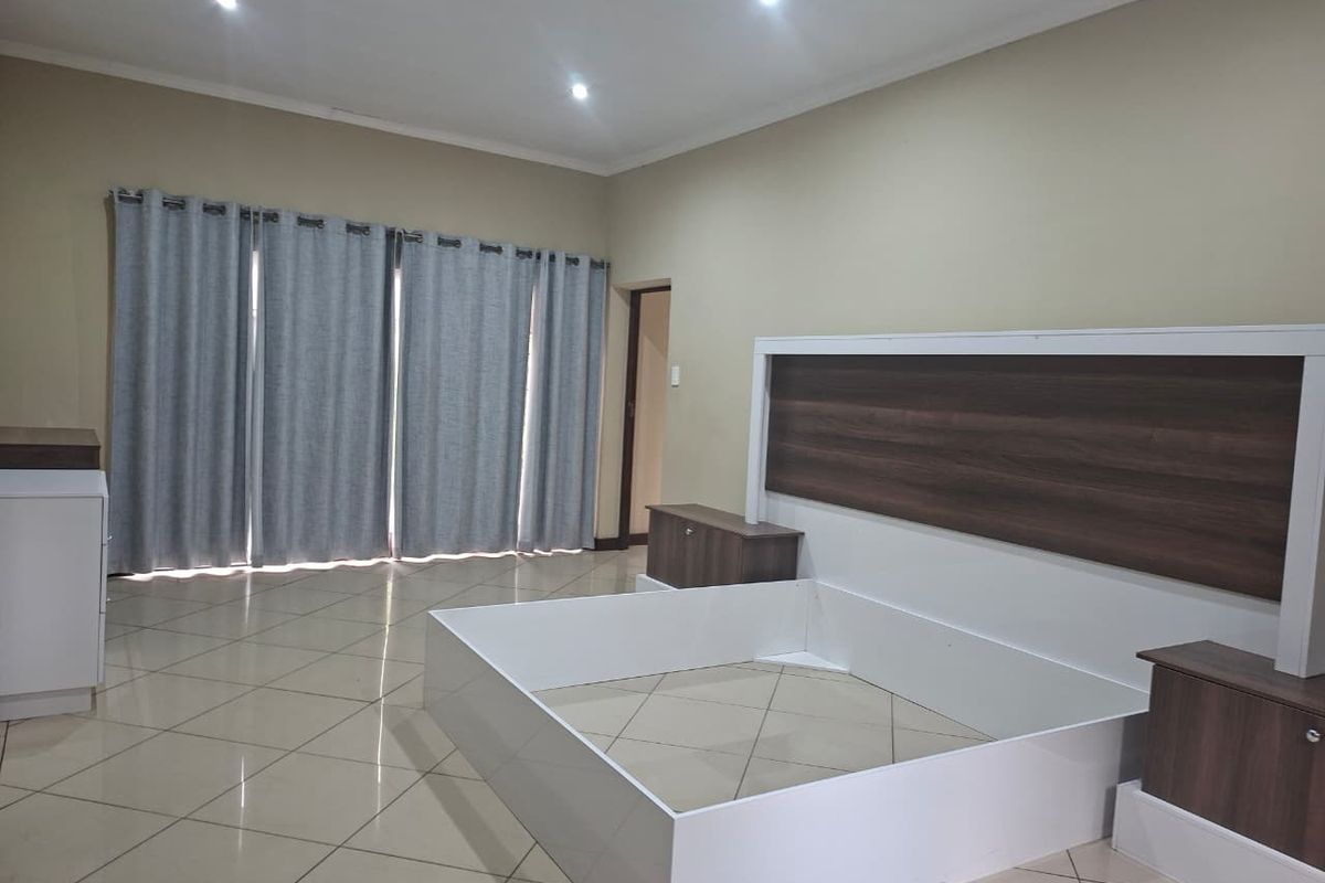 A spacious bedroom featuring neutral wall tones, large floor tiles, recessed lighting, and a built-in headboard unit.