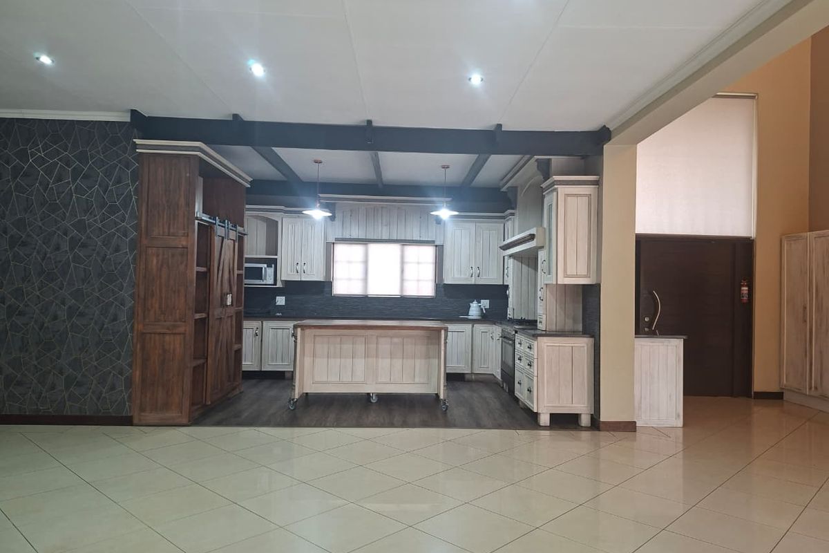 Spacious kitchen featuring custom cabinetry, a central island, built-in appliances, and exposed ceiling beams, set against a tiled open-plan living area.