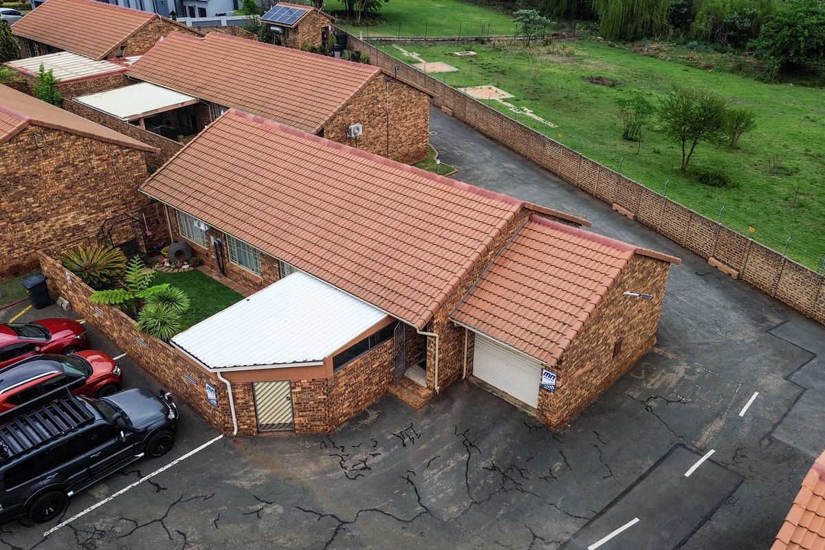 Aerial view of a face-brick townhouse featuring a tiled roof, single garage, and a paved driveway within a secure complex.