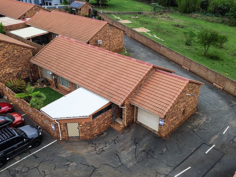 Aerial view of a face-brick townhouse featuring a tiled roof, single garage, and a paved driveway within a secure complex.