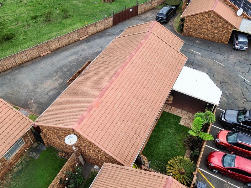 Aerial view of a townhouse complex featuring tiled roofs, brick construction, paved driveways, and established garden areas.