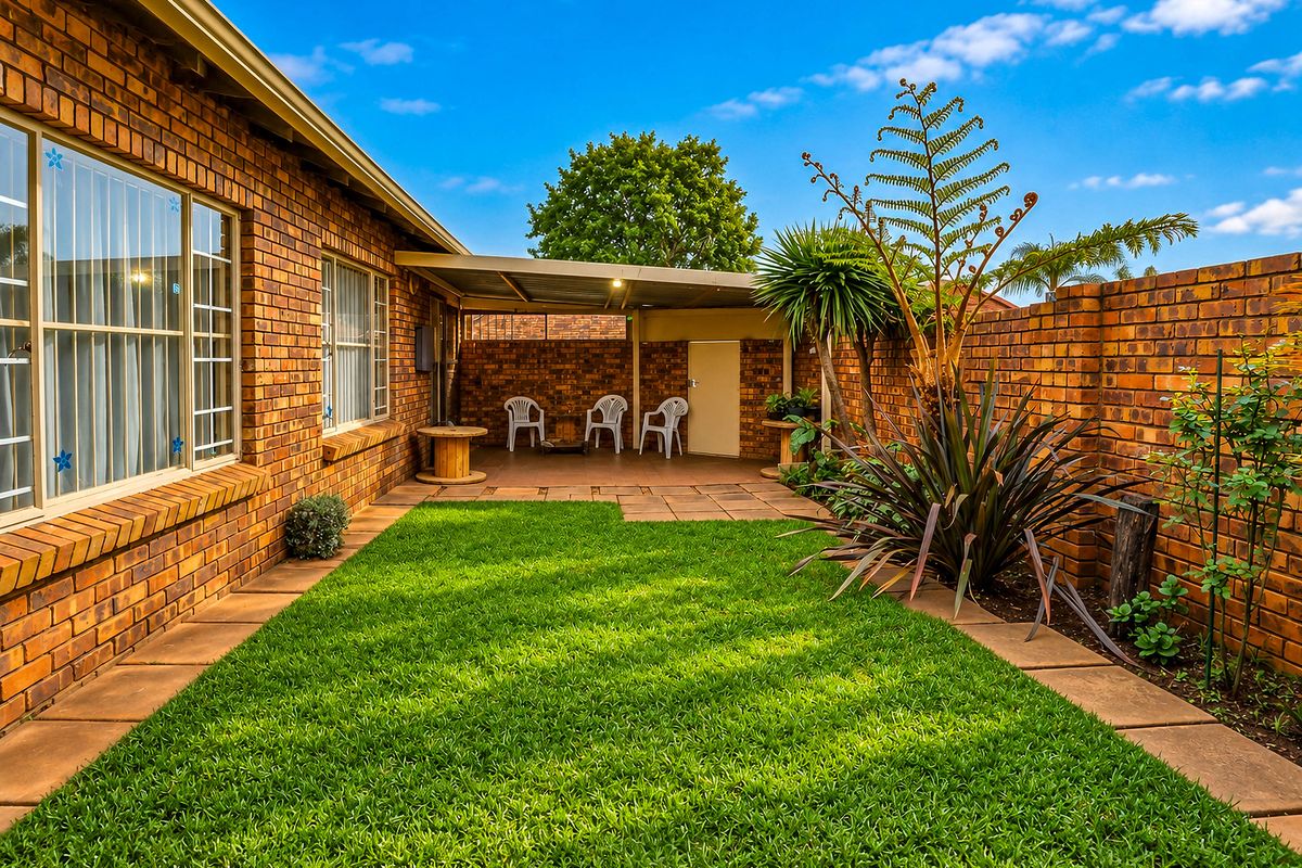 A well-maintained rear garden featuring a manicured lawn, paved pathways, and a covered patio area enclosed by brick boundary walls.