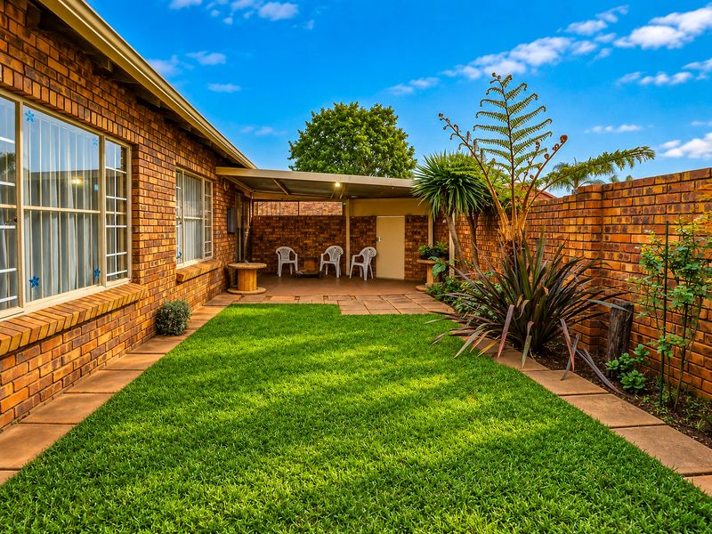 A well-maintained rear garden featuring a manicured lawn, paved pathways, and a covered patio area enclosed by brick boundary walls.
