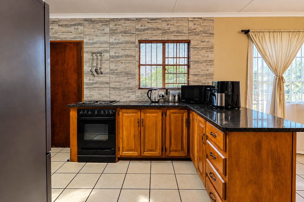 A functional kitchen featuring wooden cabinetry, granite countertops, a stone-look tiled splashback, and tiled flooring, offering a classic and practical layout.