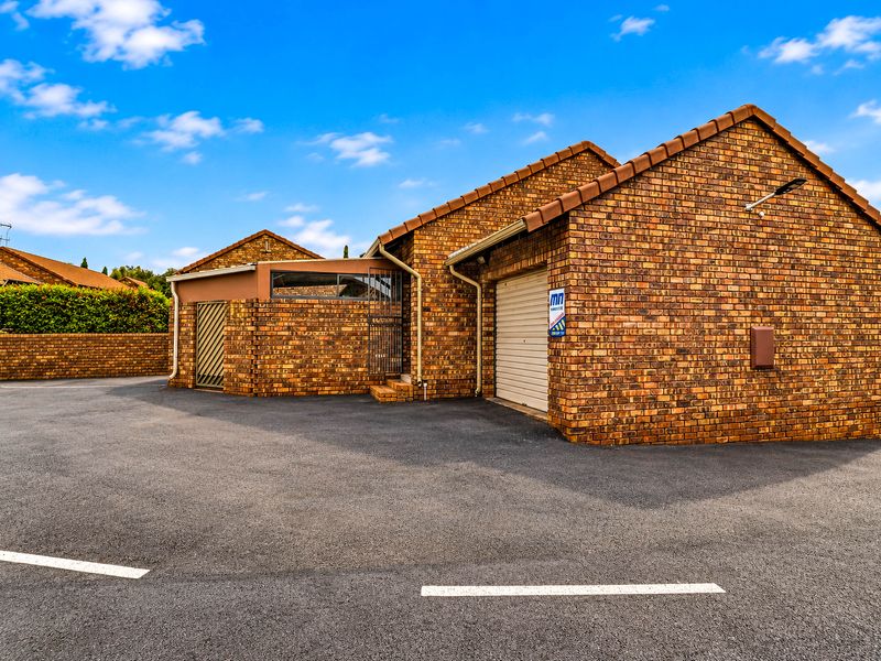 Exterior view of a face-brick townhouse featuring a tiled roof, asphalt driveway, and a secure roller garage door.