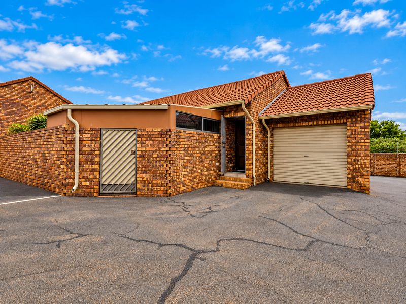 Front elevation of a face brick townhouse featuring a tiled roof, single garage with roller door, and an asphalt driveway.