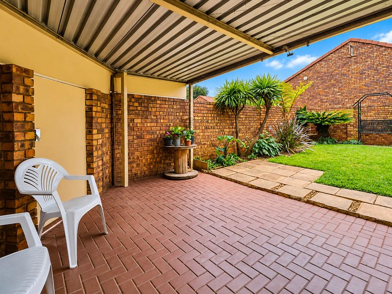 A covered patio area featuring brick paving, a corrugated metal roof, and direct access to a private garden with a brick boundary wall.