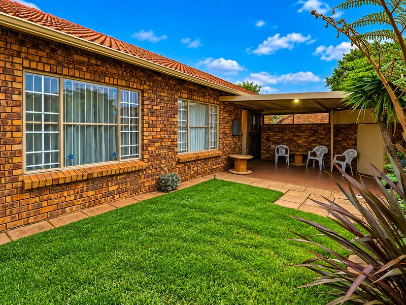 A well-maintained rear exterior view of the townhouse featuring a brick facade, a covered patio area, and a neat garden lawn.