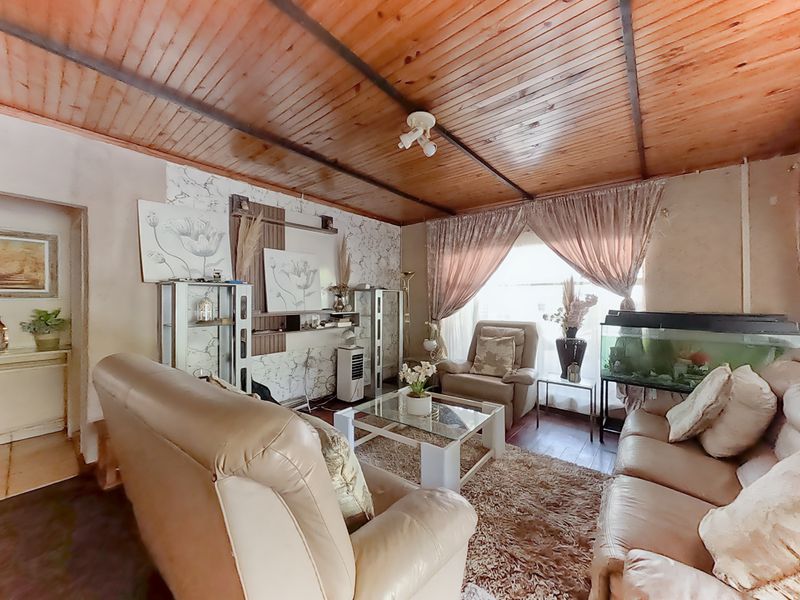 A living room featuring a timber-clad ceiling and laminate flooring, offering a dated aesthetic with potential for modernization.