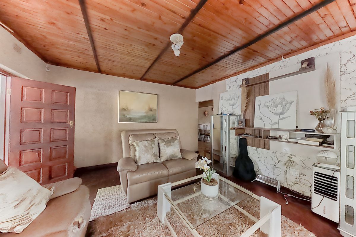 A living room featuring a timber-clad ceiling and a built-in shelving unit, offering a dated aesthetic with potential for modernization.