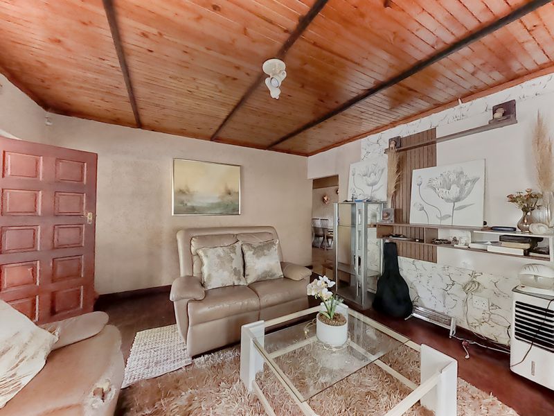 A living room featuring a timber-clad ceiling and a built-in shelving unit, offering a dated aesthetic with potential for modernization.