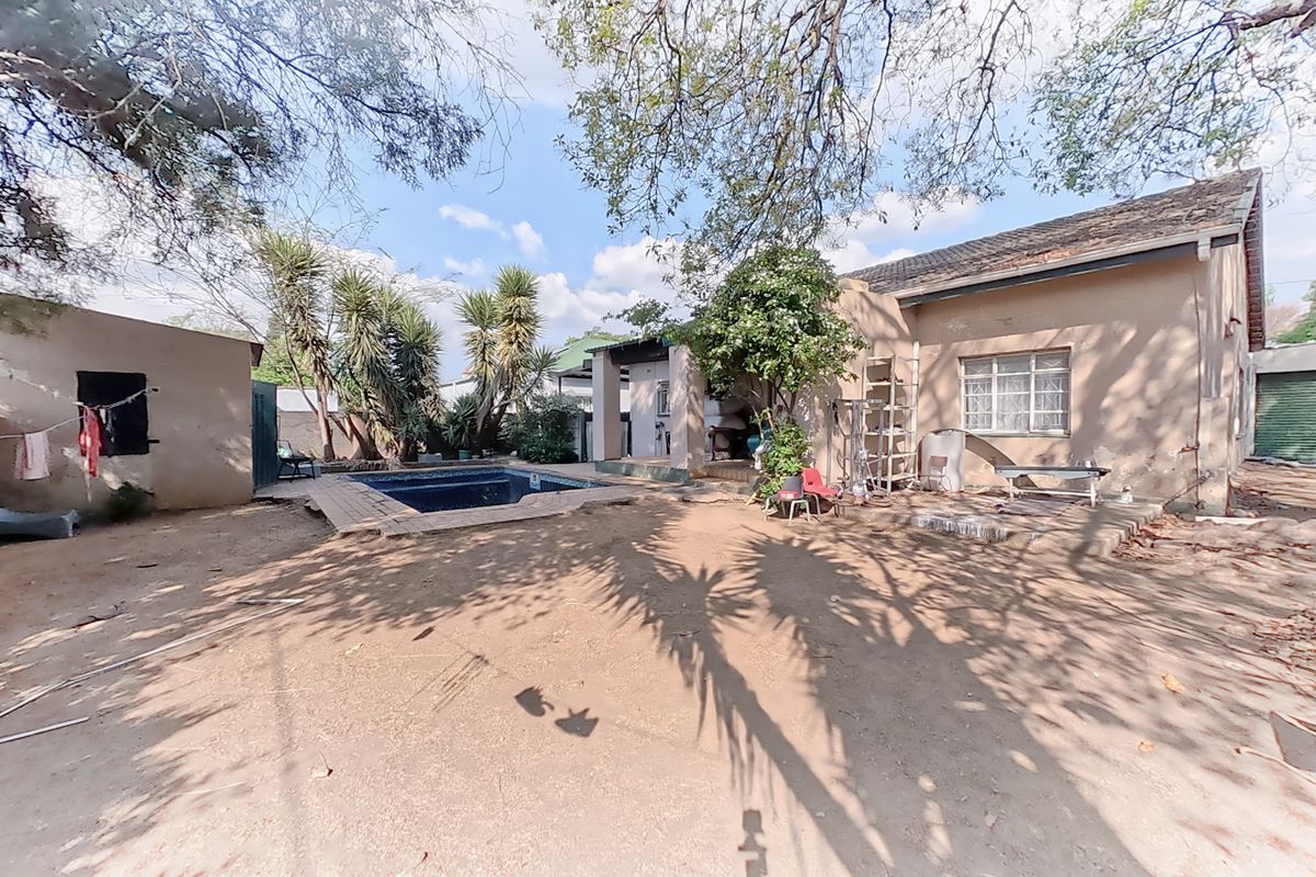 Rear exterior view of the property featuring a swimming pool, paved area, and access to the garage and main house structure.