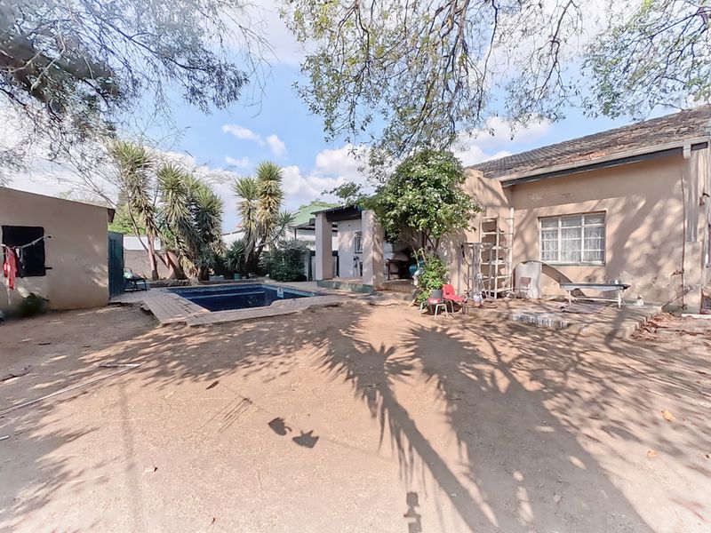 Rear exterior view of the property featuring a swimming pool, paved area, and access to the garage and main house structure.