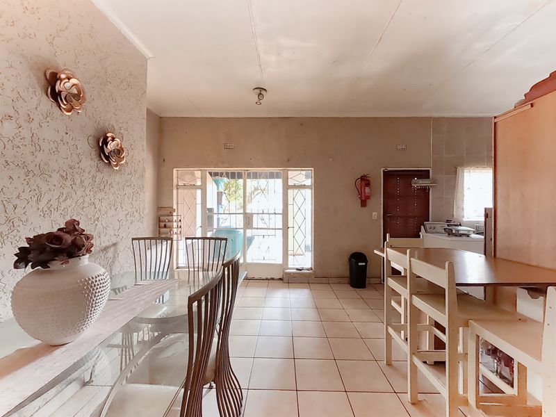 Open plan living and dining area featuring tiled flooring, a textured feature wall, and direct access to the exterior through a security gate.