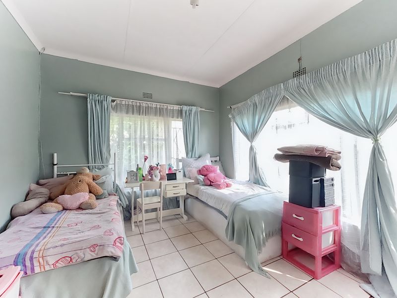 A bedroom featuring tiled flooring and large windows with curtain rails, offering a functional space with natural light.
