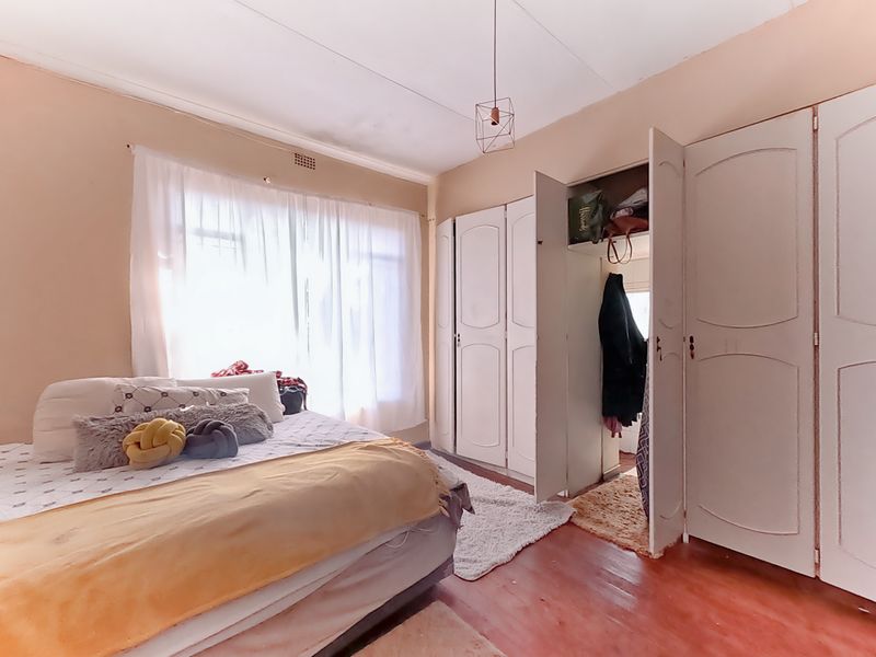 A bedroom featuring built-in cupboards and hardwood flooring, requiring cosmetic updates to the ceiling and floor finishes.