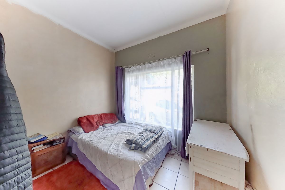 A bedroom featuring tiled flooring and a large window with a curtain rail, currently showing signs of wear on the wall finishes.