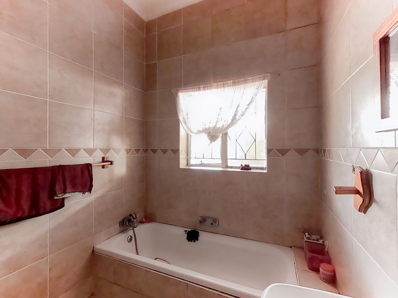 A functional bathroom featuring a built-in bathtub, full-height wall tiling, and a window with security bars.