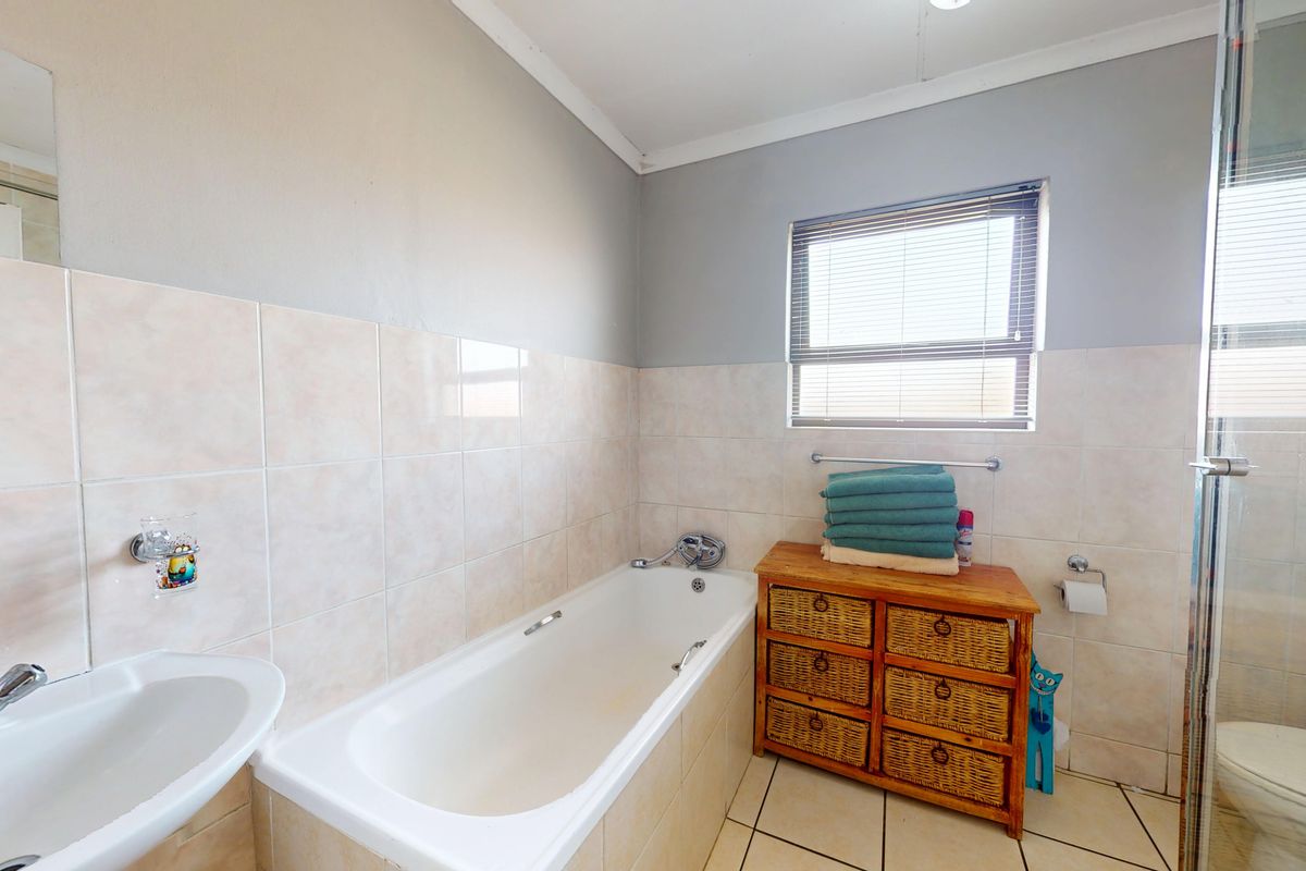 A functional bathroom featuring a bathtub, separate shower enclosure, basin, and toilet with neutral wall tiling and tiled flooring.