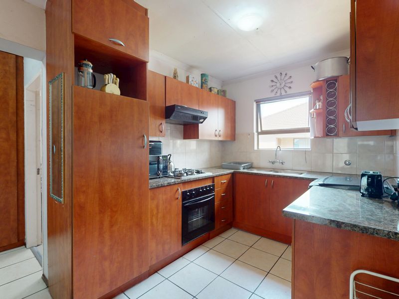 A functional kitchen featuring wood-finish cabinetry, granite-look laminate countertops, a built-in oven with gas hob, and tiled flooring throughout.