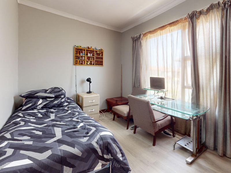 A functional bedroom featuring light-toned laminate flooring, neutral wall finishes, and a large window that provides ample natural light.