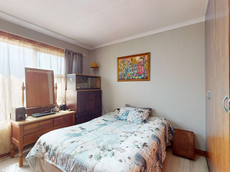 A functional bedroom featuring light-toned laminate flooring, a built-in wardrobe, and a large window allowing for natural light.