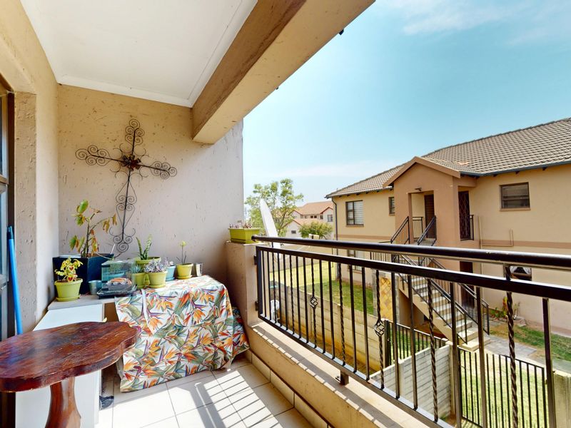 A covered balcony featuring tiled flooring and a metal balustrade, offering an outdoor space overlooking the complex grounds.