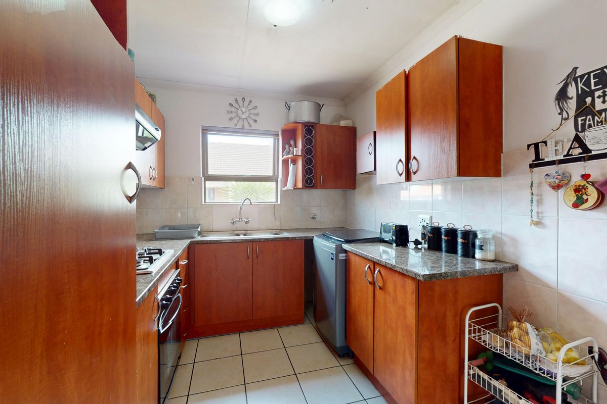 A functional kitchen featuring wood-finish cabinetry, granite-look laminate countertops, a gas hob, built-in oven, and tiled flooring.