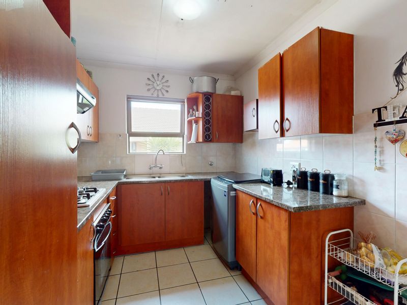 A functional kitchen featuring wood-finish cabinetry, granite-look laminate countertops, a gas hob, built-in oven, and tiled flooring.