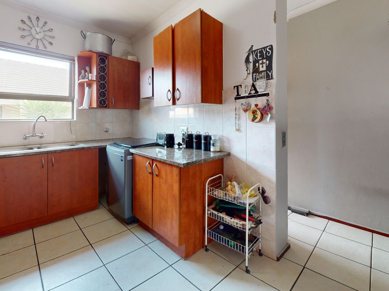 A functional kitchen featuring wood-look laminate cabinetry, granite countertops, tiled backsplash, and ceramic floor tiles, offering a practical layout for daily use.