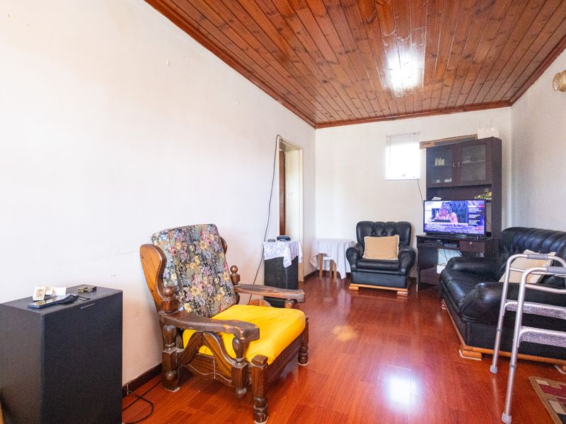 Living room featuring timber panelled ceilings and laminate flooring, offering a dated interior space ready for modernisation.