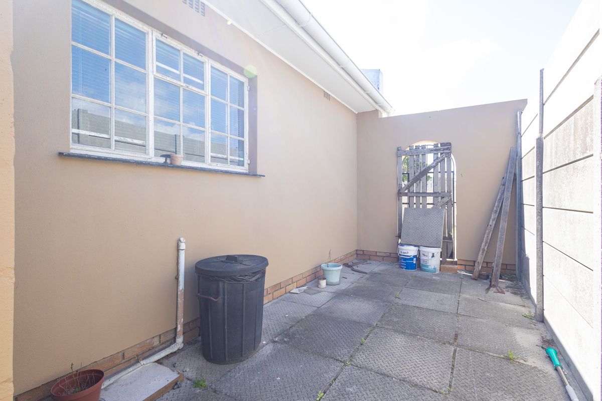 A paved rear courtyard area featuring a timber gate, boundary wall, and exterior window access.