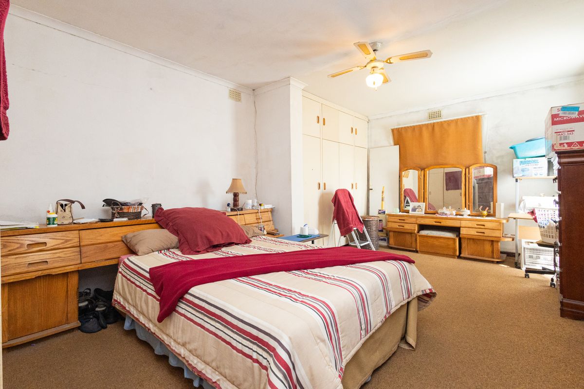 Spacious bedroom featuring built-in cupboards, a ceiling fan, and carpeted flooring, offering a functional layout with potential for cosmetic updates.