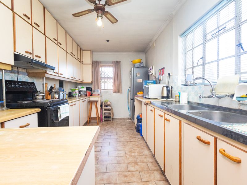 A functional kitchen featuring extensive laminate cabinetry, double bowl sink, tiled flooring, and a ceiling fan, offering potential for modernization.
