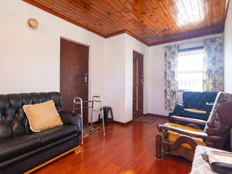 A living room featuring a timber-paneled ceiling, laminate flooring, and solid wood doors, offering a traditional layout with natural light.