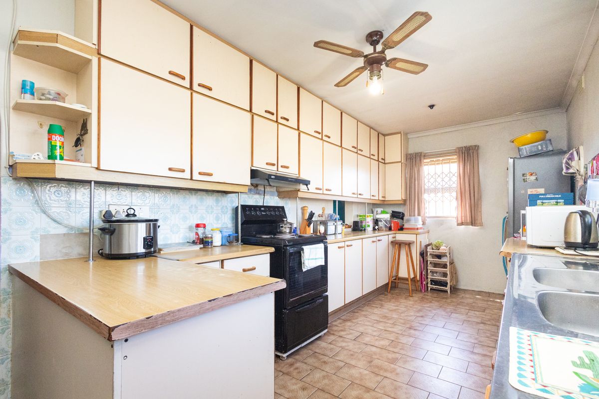 A functional kitchen featuring extensive built-in cabinetry, laminate countertops, a freestanding stove with extractor fan, and tiled flooring throughout.