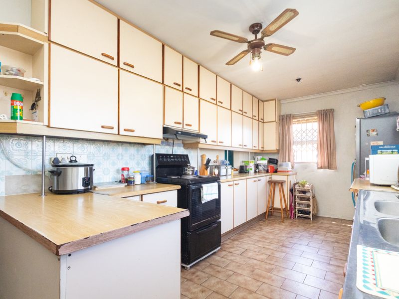 A functional kitchen featuring extensive built-in cabinetry, laminate countertops, a freestanding stove with extractor fan, and tiled flooring throughout.