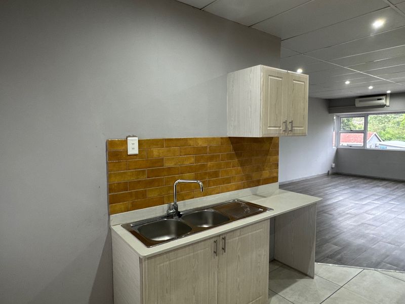 A compact, modern kitchen area featuring a stainless steel double sink, tiled backsplash, and built-in cabinetry, seamlessly integrated into an open-plan living space.