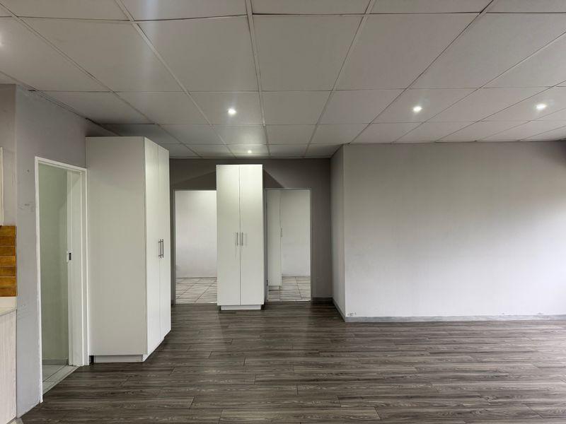 An empty living area featuring dark laminate flooring, a drop ceiling with recessed lighting, and built-in white cupboards.